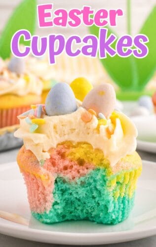 A pastel cupcake with a bite taken out, showing blue, pink, and yellow layers under buttercream frosting. Mini chocolate eggs sit on top. A pink and white text overlay reads "Easter Cupcakes."